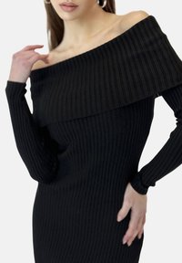 Schwarzes, geripptes Kleid mit schulterfreiem Design und langen Ärmeln, das aus einem strukturierten Stoff besteht und eine enge Passform hat, die die Silhouette betont.