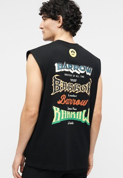 Νέος άνδρας με σγουρά σκουρόχρωμα μαλλιά που φοράει αμάνικο μαύρο πουκάμισο με πολύχρωμο στυλιζαρισμένο κείμενο «Barrow» και γραφικά σχέδια στην πλάτη.