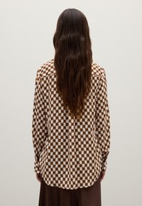 Bruine en witte gestreepte lange mouwen shirt met een gebogen zoom en knoop manchetten, met een zachte textuur en een relaxte pasvorm.