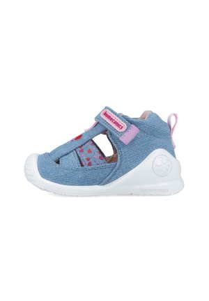 Zapatos de mezclilla azul con acentos rosas, lados abiertos, patrón de corazones, correa de Velcro y suela blanca, diseñados para la comodidad y la transpirabilidad.