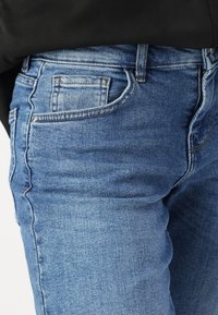 Slim-fit džínsy vyrobené z svetlomodrého denimu s miernym opotrebovaním, s klasickými vreckami a viditeľnými švovými akcentmi.