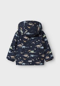 Jachetă de ploaie de culoare bleumarin, cu un model de dinozauri, cu glugă și un finisaj texturat. Include un eticheta de țesătură în partea inferioară frontală.