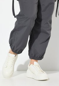 Witte platform sneakers met een gestructureerde afwerking, ronde neus en vetersluiting. Gecombineerd met tapered grijze broek met elastische boorden.