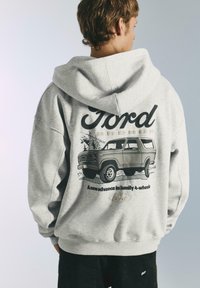 Felpa grigia con cappuccio che presenta una grafica di una Ford Bronco sul retro, con testo nero e uno stile illustrativo vintage. Cappuccio con coulisse e maniche lunghe.