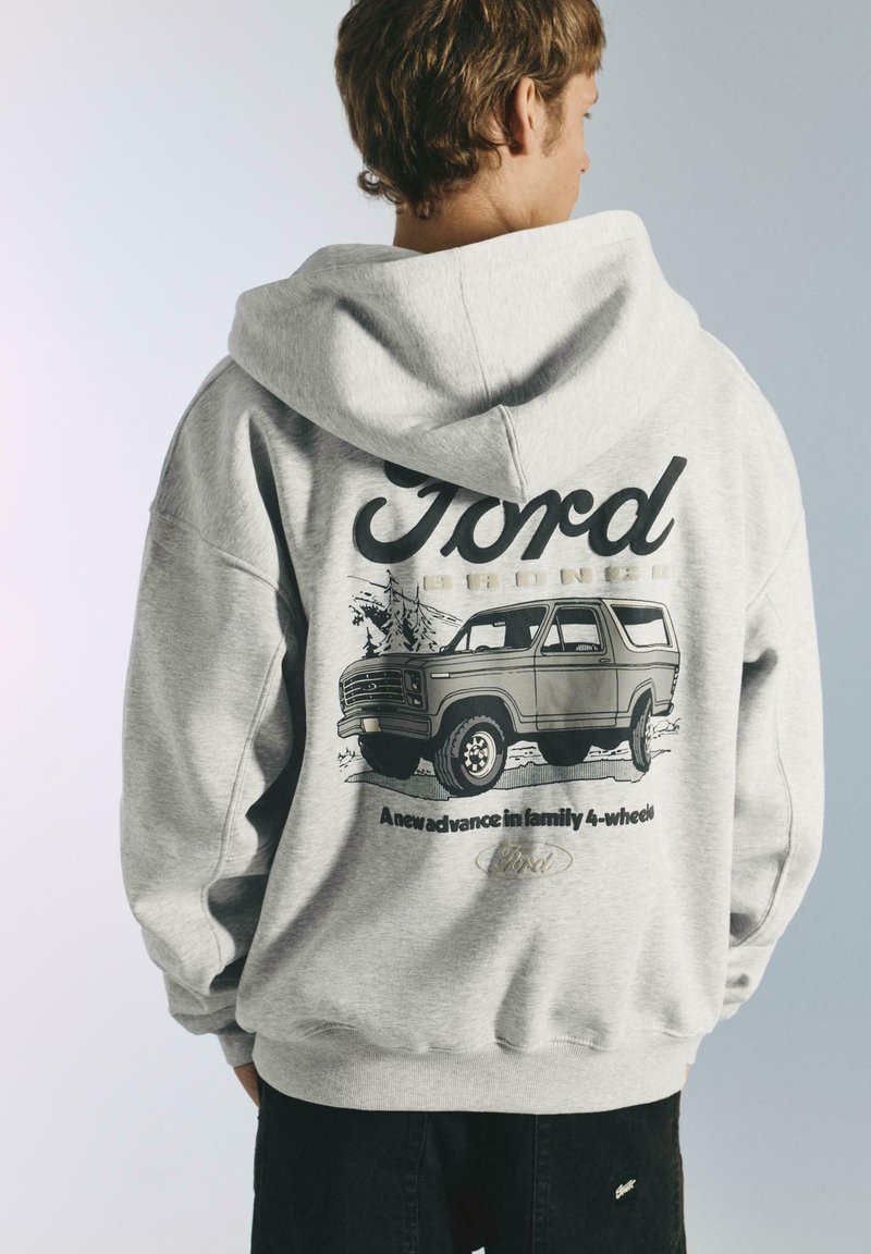 Felpa grigia con cappuccio che presenta una grafica di una Ford Bronco sul retro, con testo nero e uno stile illustrativo vintage. Cappuccio con coulisse e maniche lunghe.
