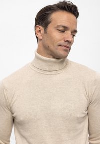 Beżowy sweter z golfem wykonany z delikatnej dzianiny. Posiada ściągacz przy kołnierzu oraz dopasowany krój. Miękka faktura z subtelnymi wariacjami kolorystycznymi.