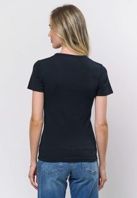 Musta ribbineuloksinen t-paita, jossa on lyhyet hihat ja pyöreä pääntie, vartalonmyötäinen malli, yhdistetty sinisten farkkujen kanssa, minimalistinen tyyli, teksturoitu kangas.