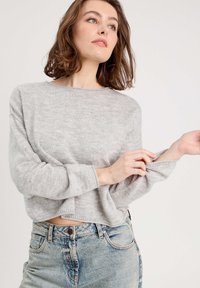 Top de punto gris de manga larga con escote redondo y hombros caídos. Combinado con jeans de mezclilla azules de talle alto, que muestran un ajuste relajado.
