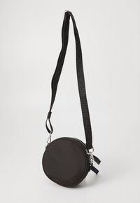 Borsa rotonda nera realizzata in materiale morbido, dotata di chiusura con zip, hardware in argento e una tracolla con il logo "HUGO" in nero.