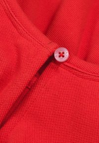 Czerwona tkanina o teksturowanym splocie, z małym różowym guzikiem o okrągłym wzorze i czterema otworami, przyszytym przy dekolcie.