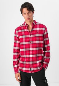 Camisa de manga larga a cuadros rojos con Acabados en blanco y negro, cierre frontal con botones, un bolsillo en el pecho y un diseño de corte relajado.