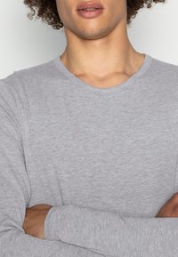 Light gray long-sleeve t-shirt with a round neckline. Soft texture, simple design, no visible patterns or accents on the fabric.