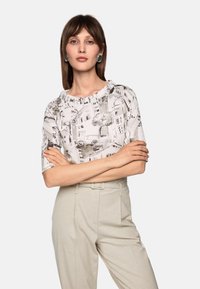 Short-sleeve white blouse with a sketch pattern featuring buildings and trees. Paired with light beige high-waisted trousers.