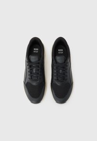 Black sneakers with mesh and leather upper, featuring round-toe design, lace-up closure, and light-colored rubber sole. Brand name visible inside.