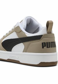 Beige és fekete sportcipő, textúrált bőr felsőrésszel, fehér középtalppal és nagy "PUMA" logóval a sarkán. Fehér fűzőkkel és gumitalppal rendelkezik.