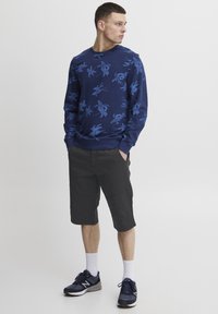 Sweatshirt bleumarin cu imprimeu floral albastru, asortat cu pantaloni şort negri până la genunchi. Modelul poartă adidași bleumarin și șosete albe până la gleznă.