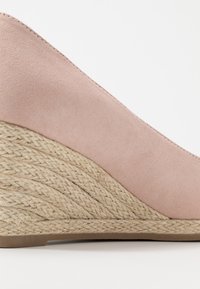 Pinky beige wigglehak met een gladde suede bovenkant en een textuur van geweven touw onderkant, met een gebogen silhouet en een vlakke beige zool.