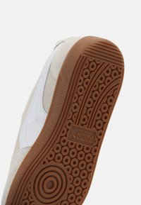 Vita mockaskor med en sula av gummirubber. Sulan har cirkulära mönster och är märkta med "Puma" och "Made in Dep." detaljer.