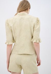 Blazer jacquard floreale giallo chiaro con maniche a sbuffo e polsini arricciati, indossato con pantaloni coordinati, mostrando un design testurizzato.