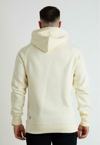 Felpa color crema con cappuccio regolabile, polsini e orlo a coste, dal design minimalista; presenta un piccolo logo vicino all'orlo.