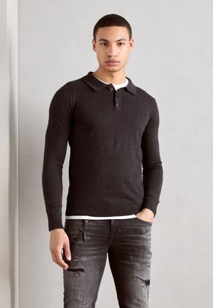 Donkergrijze langjarige polo met een kraag, vijf knopen, en geribde manchetten. Draag het over een wit T-shirt, gecombineerd met versleten jeans.