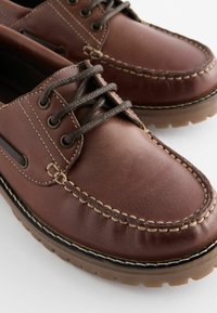 Braune Lederbootsschuhe mit runder Zehenform, kontrastierenden beigen Nähten und dunklen Schnürsenkeln. Sie verfügen über eine Gummisohle für besseren Halt.