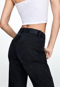 Jeans de mezclilla negros de alto talle con un acabado texturizado, que cuentan con una etiqueta de cuero en la parte posterior, bolsillos cosidos y un diseño de pierna recta.