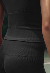 Abbigliamento sportivo nero con texture a coste, caratterizzato da un design senza cuciture e una forma aderente, che mostra la fascia in vita e una finitura del tessuto liscia.