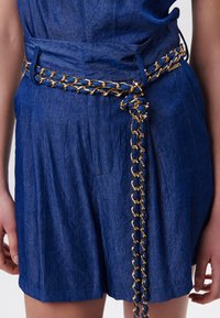 Prenda de lino azul con un acabado texturizado y diseño plisado, que cuenta con un cinturón de cadena dorada con acentos enlazados para mayor detalle.