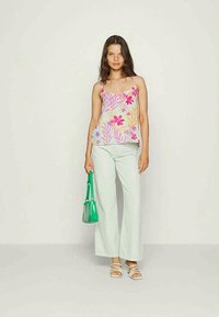 Camisola floral em rosa, amarelo e roxo sobre um fundo claro, combinada com calças largas verdes claras e uma bolsa transparente verde.