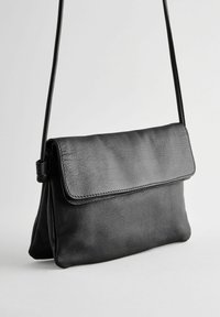 Bolso tipo bandolera de cuero negro con una textura suave, forma rectangular, solapa hacia abajo y una sola correa ajustable.