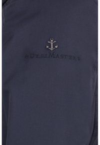 Granatowa kurtka z małym srebrnym emblematem kotwicy i wyszywanym napisem ‚DreiMaster’ poniżej. Gładki materiał o czystym wzornictwie.