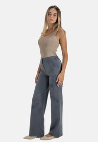 Débardeur beige à rayures associé à un pantalon gris à taille haute et à jambes larges. Chaussures plates de couleur claire. Design simple et minimaliste.