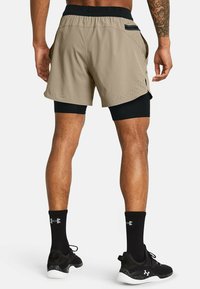 Shorts deportivos beige con capa interior negra, con perforaciones en el dobladillo y bolsillos laterales. Llevados con calcetas negras y zapatillas.