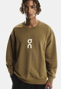 Brun sweatshirt lavet af blødt stof, med et hvidt logo på brystet, ribbede manchetter og en afslappet pasform.