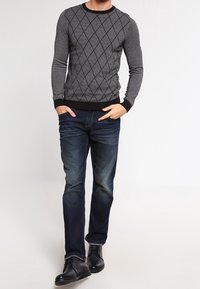 Harmaa neulepaita mustalla timanttikuviolla ja resoreilla hihansuissa, yhdistetty tummansinisiin farkkuihin ja mustiin nahkasaappaisiin.