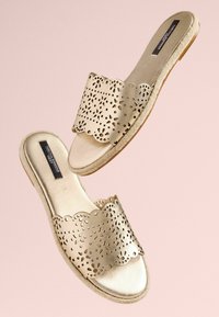 Guld læder slide sandaler med en perforeret, scalloped stropdesign og en tekstureret sål. Den overordnede form er åben til tæerne og flad.