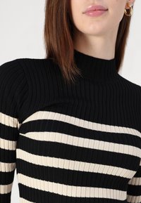Μαύρος και κρεμ ριγέ ριπ πλεχτός ζιβάγκο με εφαρμοστή σιλουέτα και υφή υφάσματος, που διαθέτει ψηλό λαιμό και οριζόντιες ρίγες.