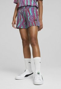 Pantalones cortos deportivos multicolores con un patrón ondulado en morado y verde azulado, combinados con calcetines blancos y zapatillas blancas con detalles en negro.