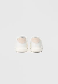 Λευκά αθλητικά παπούτσια με ανώτερο τμήμα από λείο δέρμα, σουέτ λεπτομέρειες σε ανοιχτό μπεζ στη φτέρνα και λευκή καουτσούκ σόλα. Απλός και σύγχρονος σχεδιασμός.
