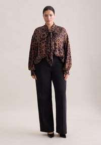 Blusa con stampa leopardata marrone e fiocco al colletto, abbinata a jeans neri a vita alta e gamba larga e décolleté neri a punta.