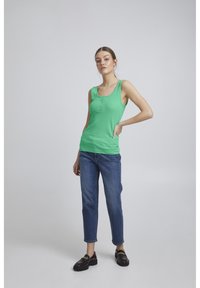 Grøn ribbet tanktop med rund halsudskæring og knapdetalje, parret med lige ben blå jeans og sorte loafers med guld accenter.
