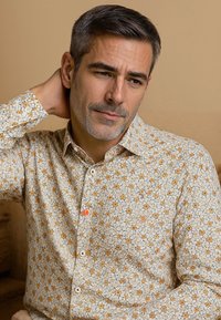 Lichtgekleurde button-up shirt met een bloemenpatroon van oranje en gele bloemen, afgewerkt met een kraag en een klein logo.