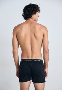 Boxeri negri cu o textură moale și un elastic pe care este inscripționat "Calvin Klein" cu text alb. Modelul este întors, punând în evidență boxeri.