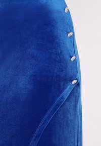 Blauer Samtstoff mit glatter Textur, der auf einer Seite mit dekorativen silberfarbenen Knöpfen verziert ist, um zusätzliche Details zu bieten.