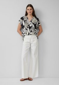 Schwarze Bluse mit kurzen Ärmeln und weißen Blattmustern, kombiniert mit hoch geschnittenen weißen weiten Hosen und braunen Sandalen.