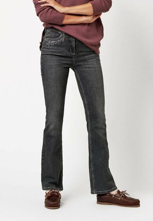 Dark denim flared jeans featuring decorative stitching on the front pockets, worn with brown leather boat shoes and a maroon sweater.