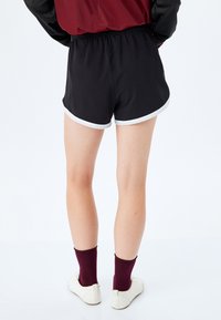 Czarne spodenki sportowe z białymi wykończeniami, elastycznym pasem i gładką tkaniną. Noszone z bordowymi skarpetkami i białymi butami.