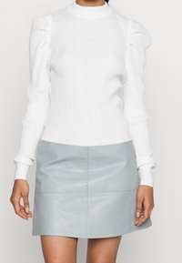 Pull en maille blanche côtelée avec col montant et manches bouffantes, associé à une mini-jupe en cuir bleu clair avec panneaux cousus.