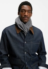 Kurtka dżinsowa z brązowym kołnierzem z sztruksu, przednimi kieszeniami i szarym wełnianym szalikiem. Kurtka zapinana na guziki, z kontrastującymi białymi mankietami koszuli.